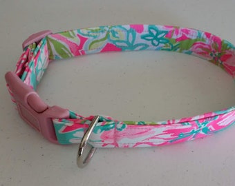 May include: A dog collar with a pink plastic buckle and a silver metal ring. The collar is patterned with a floral design in pink, green, and turquoise on a white background. The collar is approximately 1 inch wide.