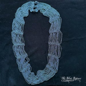 May include: A blue beaded necklace with a layered design. The necklace is made of small, round beads that are strung together in a pattern that creates a cascading effect. The necklace is a statement piece that would add a touch of elegance to any outfit.