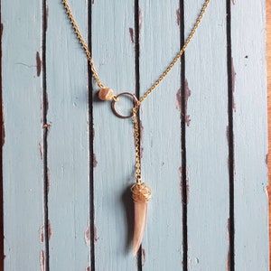 May include: A gold chain necklace with a brown shell pendant wrapped in gold wire. The pendant is shaped like a tooth or a fang. The necklace has a small brown bead and a gold circle charm.