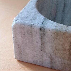 Pode incluir: Um almofariz e um pil&atilde;o de m&aacute;rmore branco com uma base quadrada e uma tigela redonda. O almofariz tem um padr&atilde;o de veios cinzentos.
