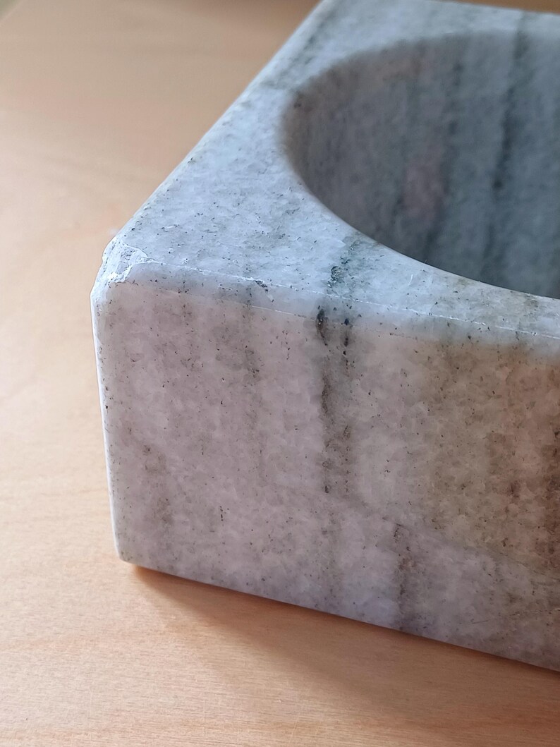 Pode incluir: Um almofariz e um pil&atilde;o de m&aacute;rmore branco com uma base quadrada e uma tigela redonda. O almofariz tem um padr&atilde;o de veios cinzentos.