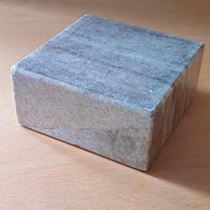 Pode incluir: Um pedestal quadrado de m&aacute;rmore cinza com uma superf&iacute;cie lisa e polida. O pedestal &eacute; feito de pedra natural e tem uma cor cinza claro com veios cinza mais escuros.