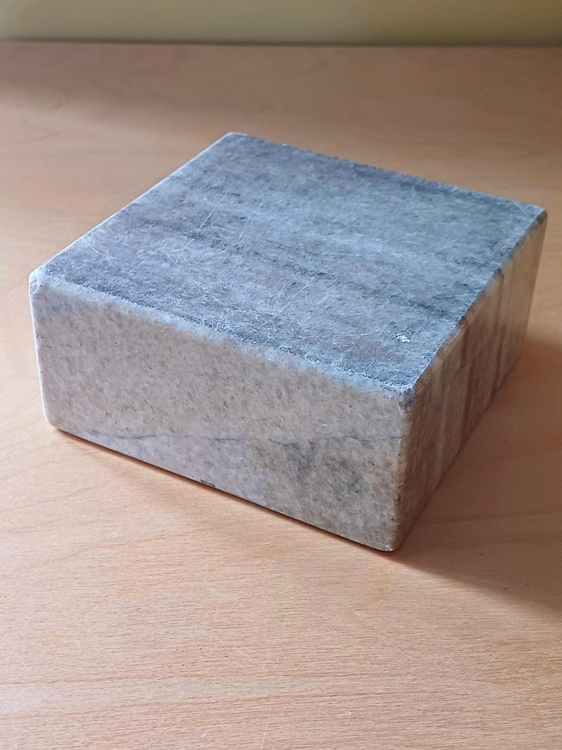 Pode incluir: Um pedestal quadrado de m&aacute;rmore cinza com uma superf&iacute;cie lisa e polida. O pedestal &eacute; feito de pedra natural e tem uma cor cinza claro com veios cinza mais escuros.