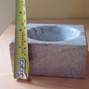 Pode incluir: Uma pequena tigela quadrada de m&aacute;rmore cinza com um interior arredondado. A tigela tem aproximadamente 10 cm de di&acirc;metro.