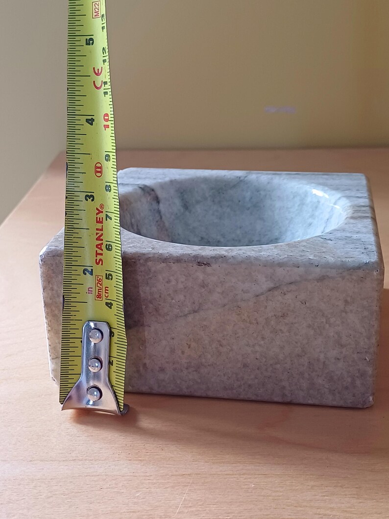 Pode incluir: Uma pequena tigela quadrada de m&aacute;rmore cinza com um interior arredondado. A tigela tem aproximadamente 10 cm de di&acirc;metro.