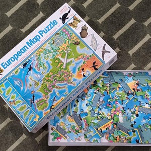 May include: A boxed European Map Puzzle with the box open, revealing the puzzle pieces. The box features a map of Europe with illustrations of animals and landmarks. The puzzle pieces are scattered in a white tray.