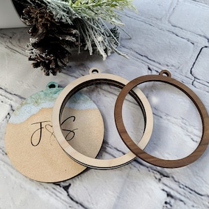 May include: Three unfinished wooden ornaments, two are round and one is round with a painted design. The round ornaments have a hole at the top for hanging. The painted ornament has the letters "J & S" written on it.
