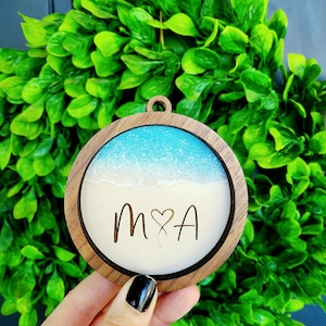 May include: A round wooden ornament with a blue and white resin beach scene and the initials "M&A" engraved in the sand.
