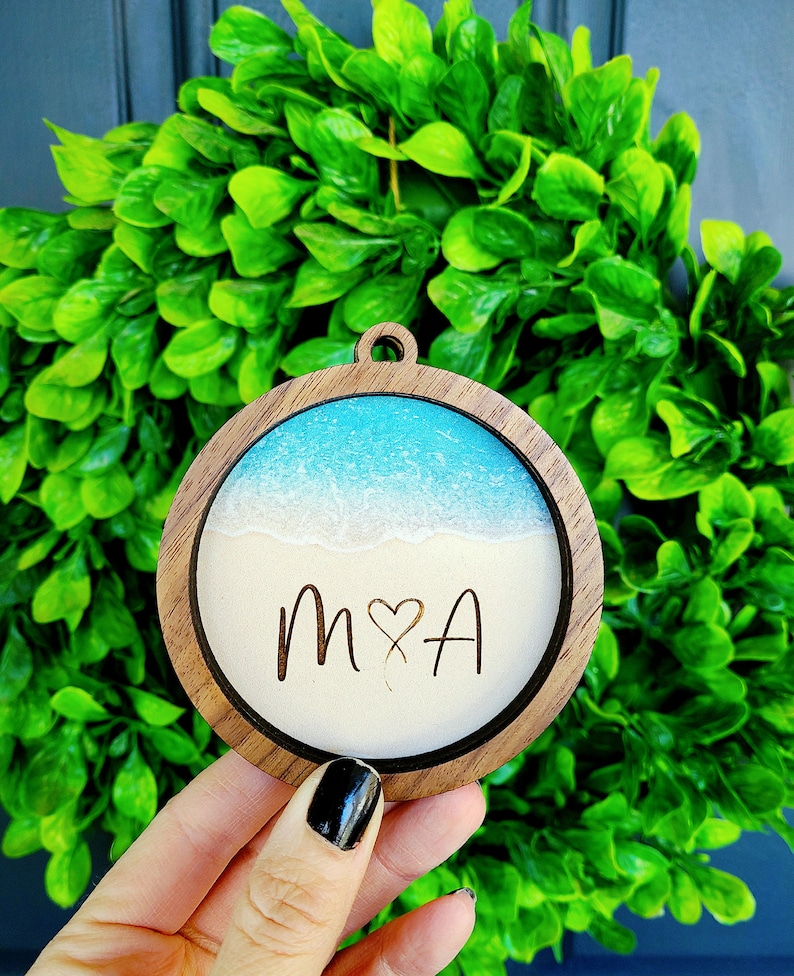 May include: A round wooden ornament with a blue and white resin beach scene and the initials "M&A" engraved in the sand.