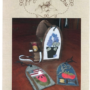 May include: A set of three felt tote bag ornaments featuring a watermelon, a tomato, and a pair of scissors. The ornaments are designed to be sewn onto a tote bag. The pattern is called "Summer Tote Adornments" and the pattern number is "LAS952".