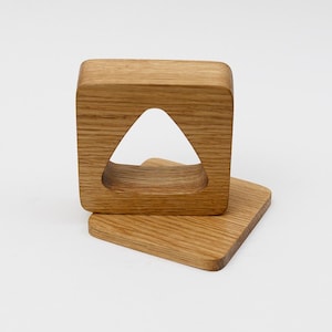 以下が含まれることがあります： 明るい木製のコースターセット。1つは三角形の切り抜きがある正方形、もう1つは長方形です。どちらも木目がはっきり見える明るい茶色の木材で作られています。ミニマルでモダンなデザインです。
