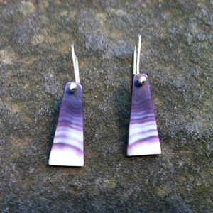 May include: A pair of silver earrings with purple and white shell accents. The earrings are a simple, elegant design.