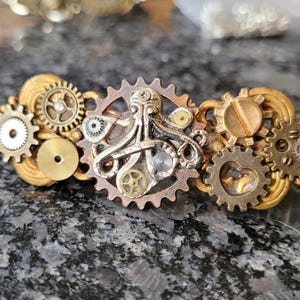May include: A gold and silver steampunk-style hair clip featuring an octopus design with gears and cogs.