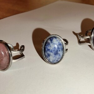 Puede incluir: Tres anillos de plata con piedras de forma ovalada. Las piedras son rosas, azules y moradas.