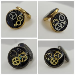 May include: Two pairs of gold cufflinks with black and gold gear designs. The cufflinks are round and have a black background with gold gears and accents.