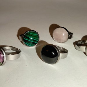 Peut inclure: Cinq bagues en argent avec des pierres de différentes couleurs. Les pierres sont vertes, roses, noires et bleues.
