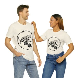 May include: Off-white t-shirts featuring a black graphic of a leopard running inside a barbed wire circle, with two dice below. The shirts are worn by a man and a woman, both in casual attire.