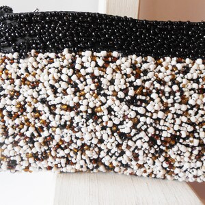 May include: A black and white beaded clutch purse with a brown accent. The purse is made of small beads sewn together in a dense pattern.