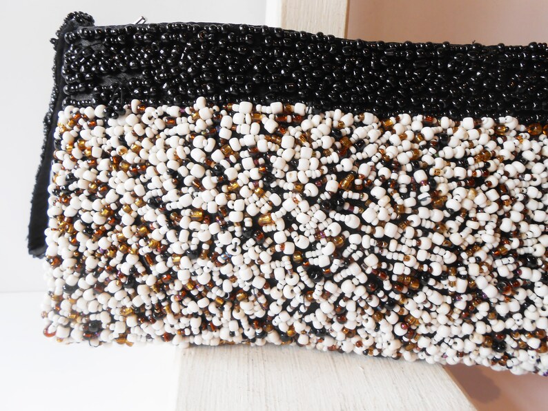 May include: A black and white beaded clutch purse with a brown accent. The purse is made of small beads sewn together in a dense pattern.