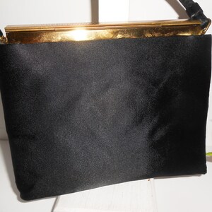 May include: A black satin evening bag with a gold metal clasp and a black braided strap.