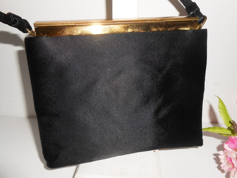 May include: A black satin evening bag with a gold metal clasp and a black braided strap.