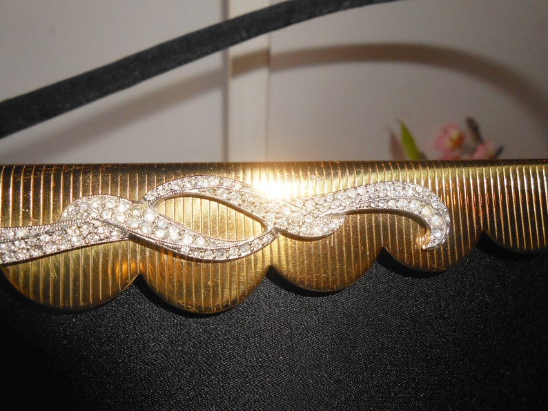 May include: A gold-colored clutch purse with a scalloped edge and a rhinestone design. The rhinestone design is a wavy line with two loops.