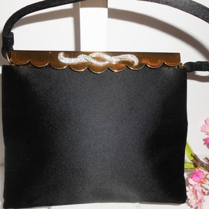 May include: A black satin evening bag with a gold clasp and a rhinestone design. The bag has a short, black handle.
