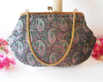 May include: Vintage paisley print handbag with a gold chain strap. The bag features a dark background with a repeating paisley pattern in shades of green, pink, and purple. The frame and clasp are gold-toned.