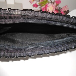 May include: A black beaded clutch purse with a zipper closure. The purse is open and the inside is lined with black fabric.