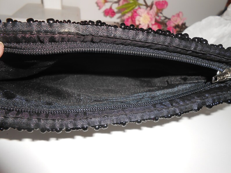 May include: A black beaded clutch purse with a zipper closure. The purse is open and the inside is lined with black fabric.