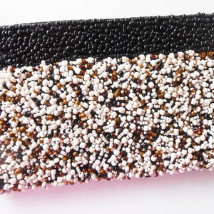 May include: A small black and white beaded clutch purse. The purse is made of small beads in black, white, and brown colors.