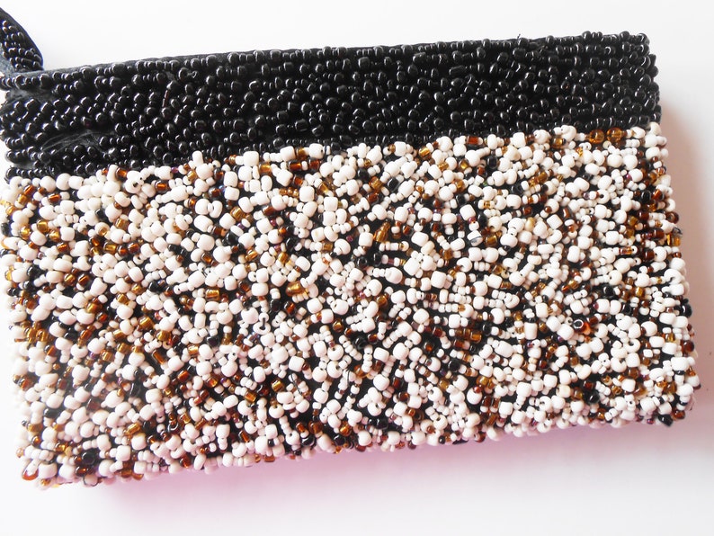 May include: A small black and white beaded clutch purse. The purse is made of small beads in black, white, and brown colors.