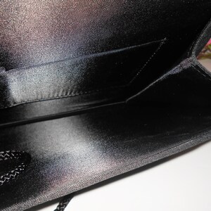May include: Black satin clutch bag with a small interior pocket. The bag has a zipper closure and a black braided cord.