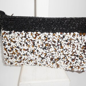 May include: A black and white beaded clutch purse with a black beaded strap. The purse has a rectangular shape and is covered in small beads.