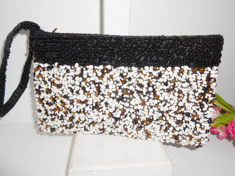 May include: A black and white beaded clutch purse with a black beaded strap. The purse has a rectangular shape and is covered in small beads.