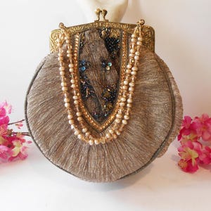 May include: A round, gold-toned clutch purse with a beaded fringe and a decorative clasp. The purse is adorned with a beaded design in the center.