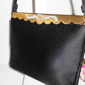 May include: A black satin evening bag with a gold metal frame and a rhinestone embellishment. The bag has a scalloped edge and a chain strap.