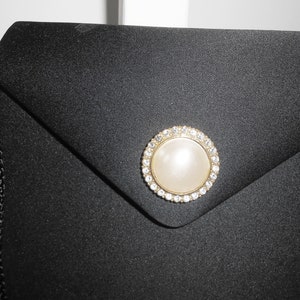 May include: A black satin evening bag with a gold and rhinestone clasp featuring a faux pearl in the center.