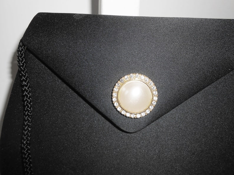 May include: A black satin evening bag with a gold and rhinestone clasp featuring a faux pearl in the center.