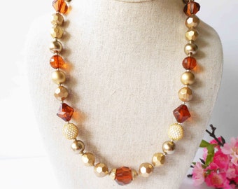 May include: A gold and amber beaded necklace with faceted and round beads. The necklace is displayed on a fabric-covered mannequin.