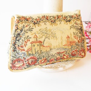 May include: A vintage tapestry clutch purse with a floral and building design. The purse is beige with red, green, and yellow accents.