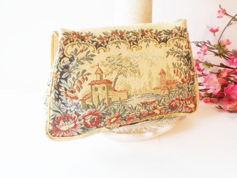 May include: A vintage tapestry clutch purse with a floral and building design. The purse is beige with red, green, and yellow accents.