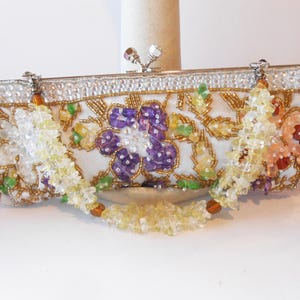 May include: A white beaded clutch purse with a floral design featuring purple, yellow, and orange beads. The purse has a silver clasp and a beaded chain strap.