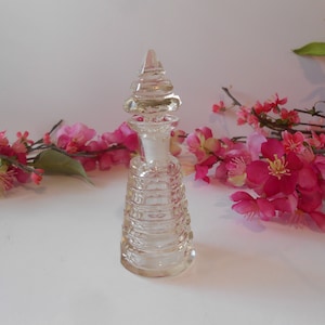 May include: A clear glass bottle with a textured, pyramid-shaped stopper. The bottle is empty and has a clear, glass base.