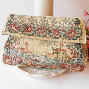 May include: A vintage tapestry clutch bag with a floral and landscape design. The bag has a flap closure and a cream background with red, green, and brown accents.