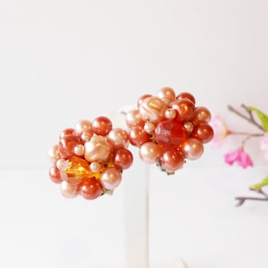 May include: A pair of clip-on earrings with a cluster of pink, orange, and peach colored beads. The earrings have a vintage style.