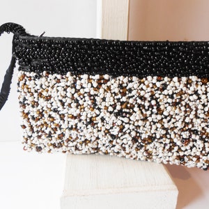 May include: A black and white beaded clutch purse with a black satin strap. The purse is made of small, round beads in a variety of colors, including white, black, and brown.
