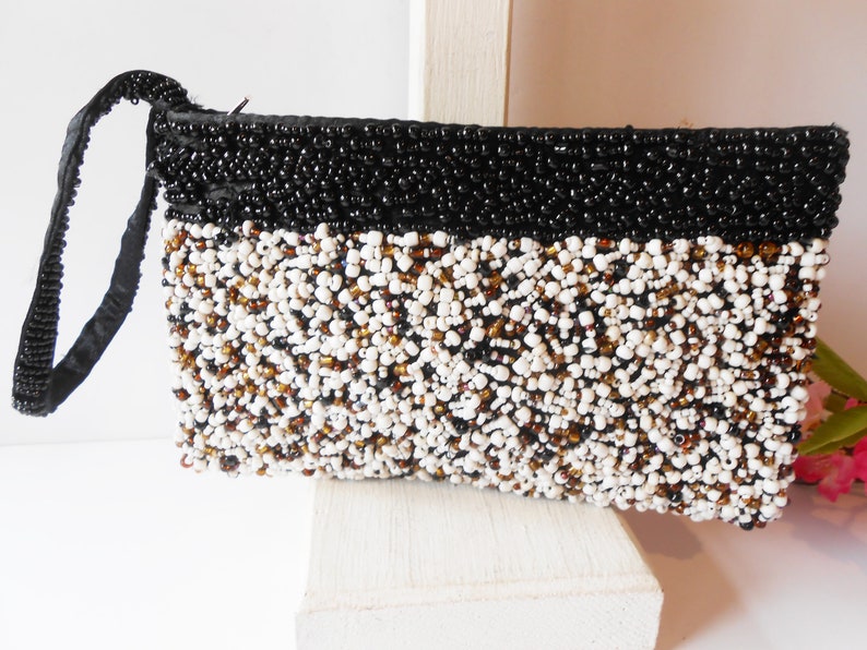 May include: A black and white beaded clutch purse with a black satin strap. The purse is made of small, round beads in a variety of colors, including white, black, and brown.