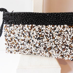 May include: A black and white beaded clutch with a black strap. The clutch is made of small, round beads in a variety of colors, including white, black, and brown.