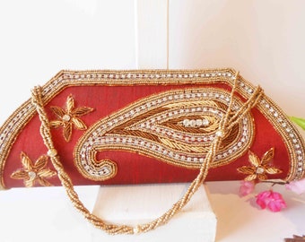Könnte beinhalten: Eine rote Perlenclutch mit einem goldenen und silbernen Paisley-Muster. Die Clutch hat einen Kettenriemen aus Perlen.